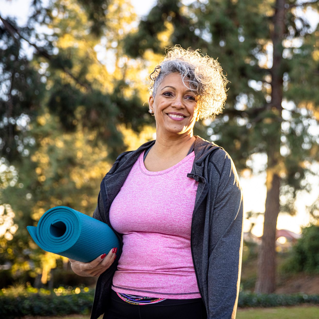 Woman holding a rolled up yoga mat outside