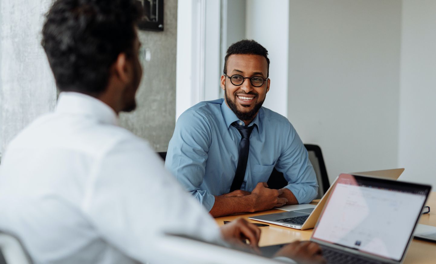 Two men sitting at a conference table with laptops smiling